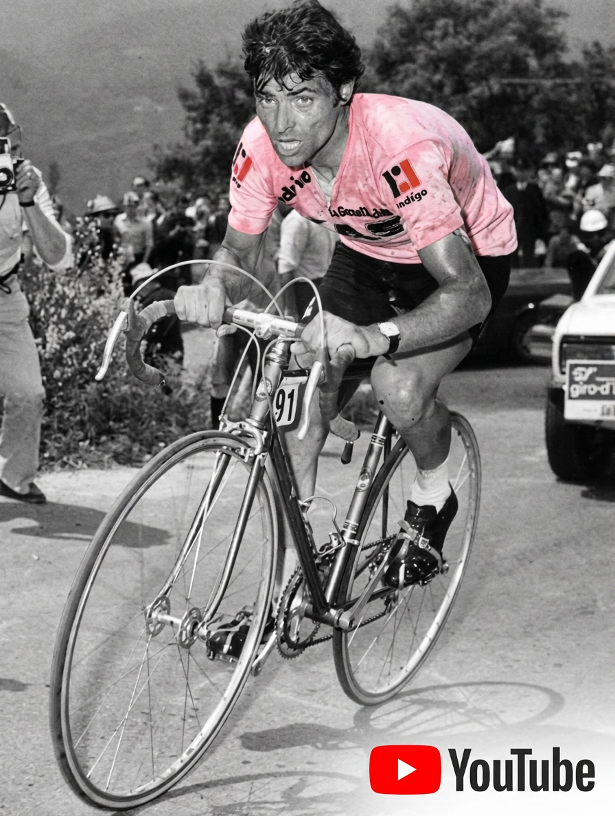 Fuente A male cyclist wearing a pink jersey pushes hard on a bicycle during a race, surrounded by spectators and equipment in a mountainous landscape.